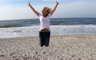 Frau am Strand macht Freuden-Luftsprung